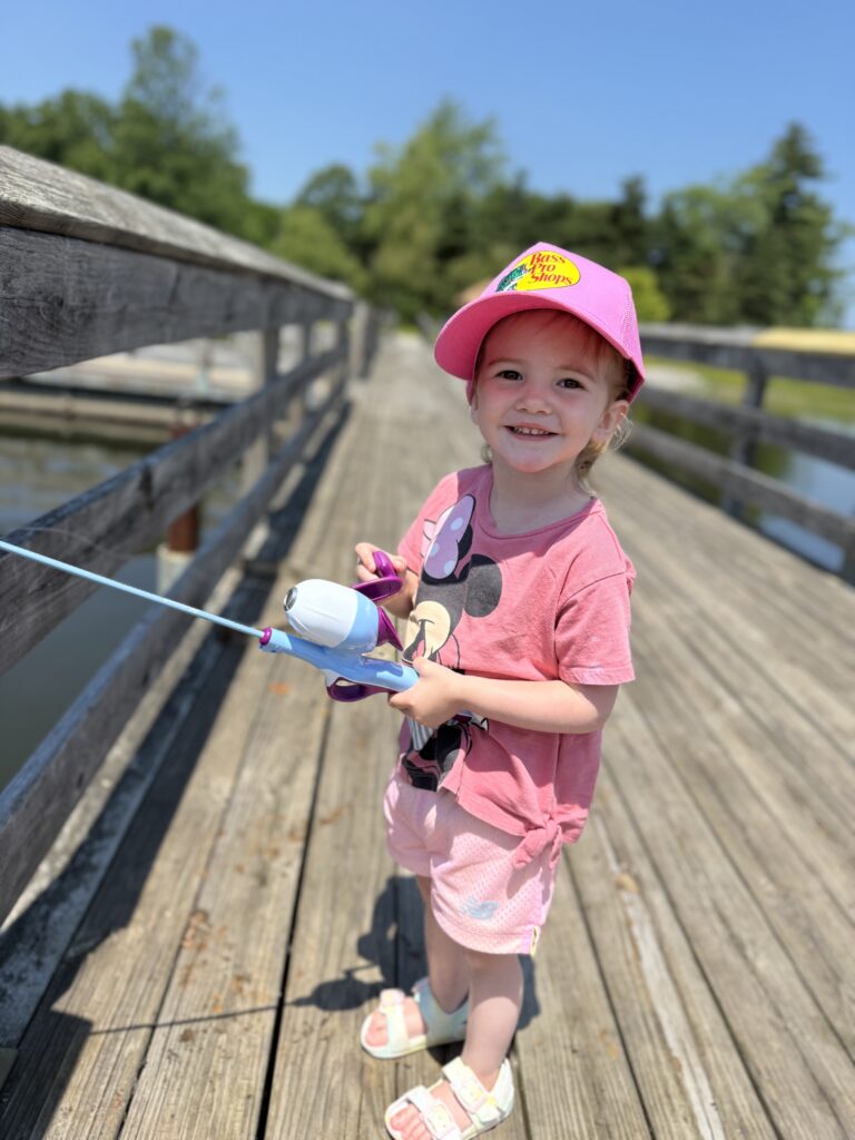 2 year old girl in all pink fishing off the side of a dock